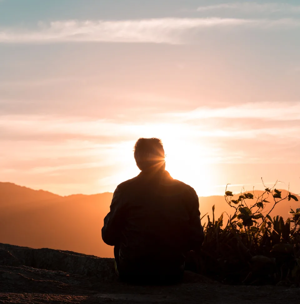 Eine Person sitzt mit Blick auf die Berge im warmen Licht des Sonnenuntergangs.